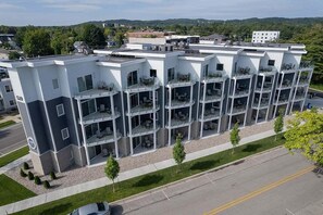 A multi-story hotel with a modern design, featuring balconies with outdoor seating and a parking lot in front. - 🌆 539 Bay St Lakeview Condo | Walk to Downtown & Beach ➠ 102W (Traverse City)