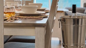 A dining area with a table set for two, a metal bucket, and a view of the ocean through large windows. - 🌆 539 Bay St Downtown Lakeview Condo | 202W - Waterfront, Free Parking, Moments from festival grounds (Traverse City)