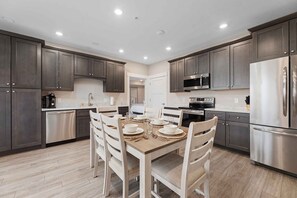 A modern kitchen with dark cabinets, stainless steel appliances, and a dining area set for four.