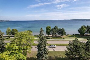 A coastal view with a road, trees, and a body of water. - 539 Bay St Lakeview Condo | 204E - Waterfront & Free Parking  204E (Traverse City)