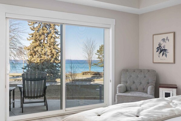 A bedroom with a sliding glass door leading to a balcony with a view of a lake and trees. - 539 Bay St Lakeview Condo | 204E - Waterfront & Free Parking 204E (Traverse City)