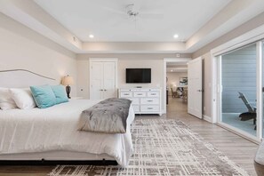 A bedroom with a bed, a dresser, a TV, and a sliding glass door leading to a balcony.