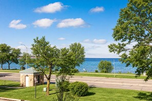 A coastal road with a small stone building, trees, and a clear view of the sea. - 539 Bay St Lakeview Condo | 204E - Waterfront & Free Parking  204E (Traverse City)
