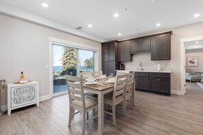 A modern kitchen with dark cabinets, a dining area with a table set for four, and a view of the outdoors through a sliding glass door. - 539 Bay St Lakeview Condo | 204E - Waterfront & Free Parking 204E (Traverse City)
