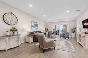 A spacious living room with a large clock, a fireplace, and a television. - 539 Bay St Lakeview Condo | 204E - Waterfront & Free Parking 204E (Traverse City)