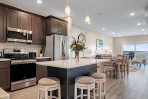 A modern kitchen with stainless steel appliances, a large island with stools, and a dining area with a view.