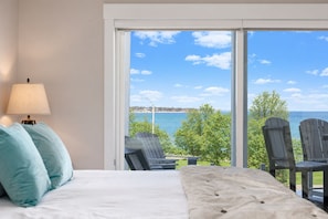 A bedroom with a large window, a bed with pillows, and two chairs facing the window.