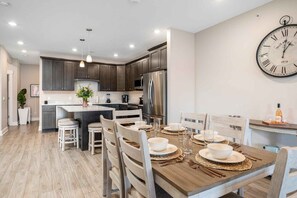 A modern kitchen with dark cabinets, stainless steel appliances, and a dining area with a wooden table set for four.