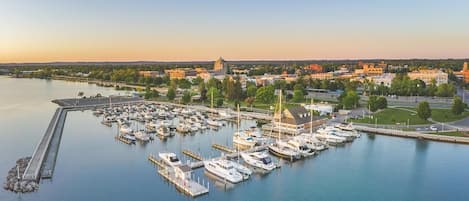 A marina with boats docked, a pier extending into the water, and buildings in the background.