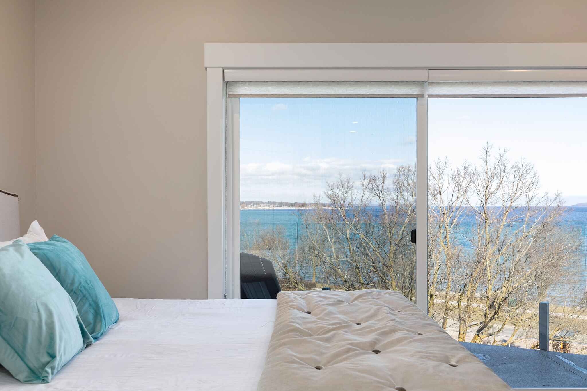 A bedroom with a bed, pillows, and a large window with a view of trees and water.