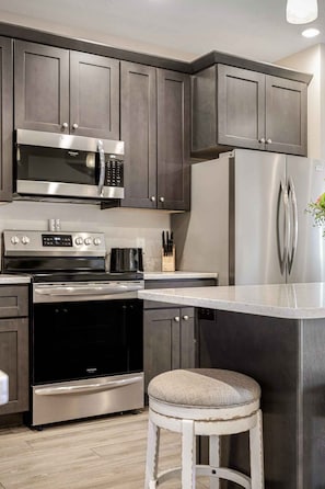 A modern kitchen with stainless steel appliances, dark wood cabinets, and a white island with a cushioned stool. - 539 Bay Penthouse Suite | Panoramic Bayviews 403E (Traverse City)