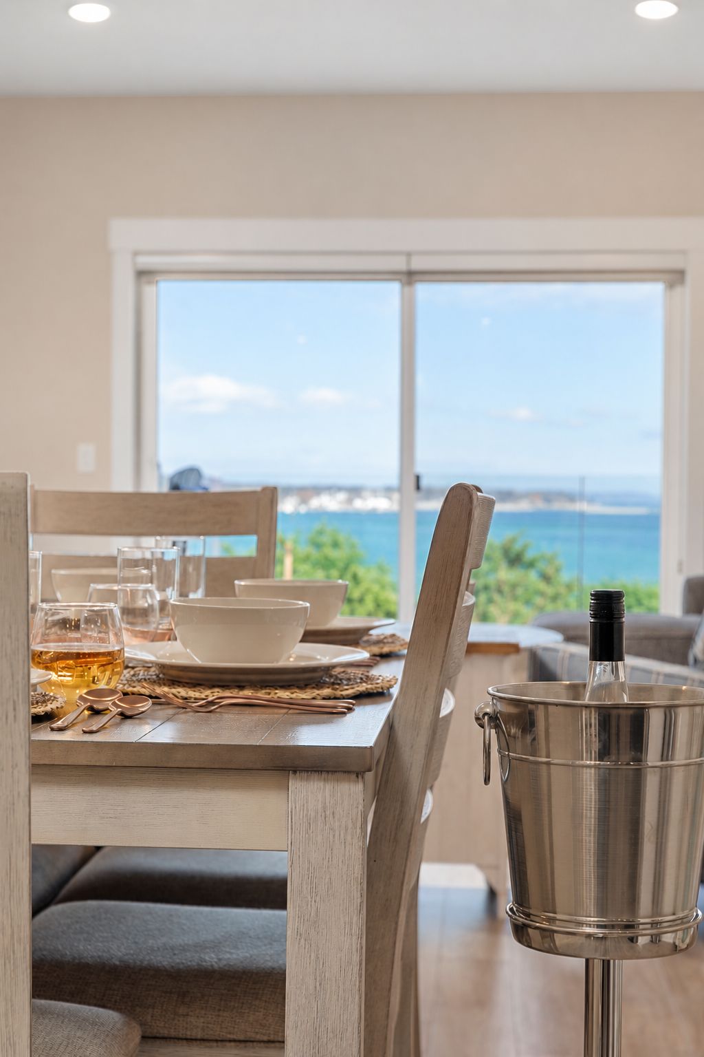 A dining area with a view of the ocean, a table set with glasses and bowls, and a metal container on the table.