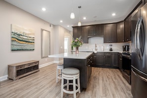 Pale island with stools and a flower arrangement in a kitchen with dark wood cabinetry. - 539 Bay Penthouse Suite | Panoramic Bayviews 402W (Traverse City)