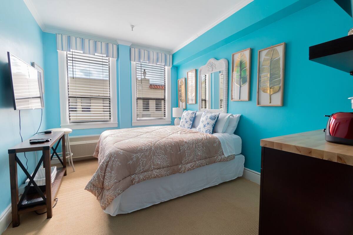 A bedroom with a bed, a desk, a chair, and a TV.