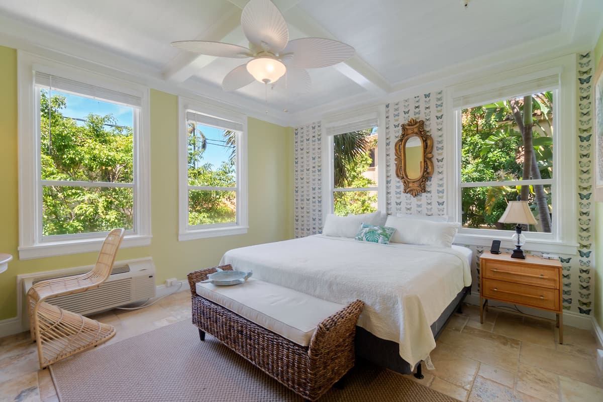 A bedroom with a large bed, a ceiling fan, and a window with a view of trees.