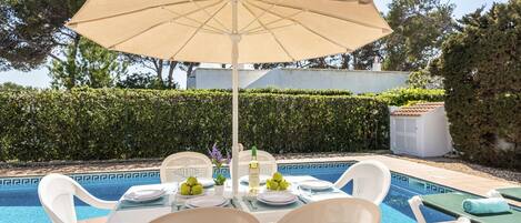 Un espace repas aménagé au bord de la piscine, avec une table, des chaises et un parasol.