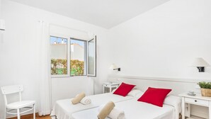 Een schone, witte kamer met twee bedden, rode kussens en een witte stoel.