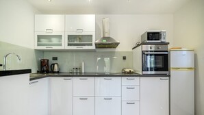 A modern kitchen with white cabinets, a stainless steel range hood, a built-in oven, a microwave, and a refrigerator. - Holiday Home Rokoko (Sibenik)