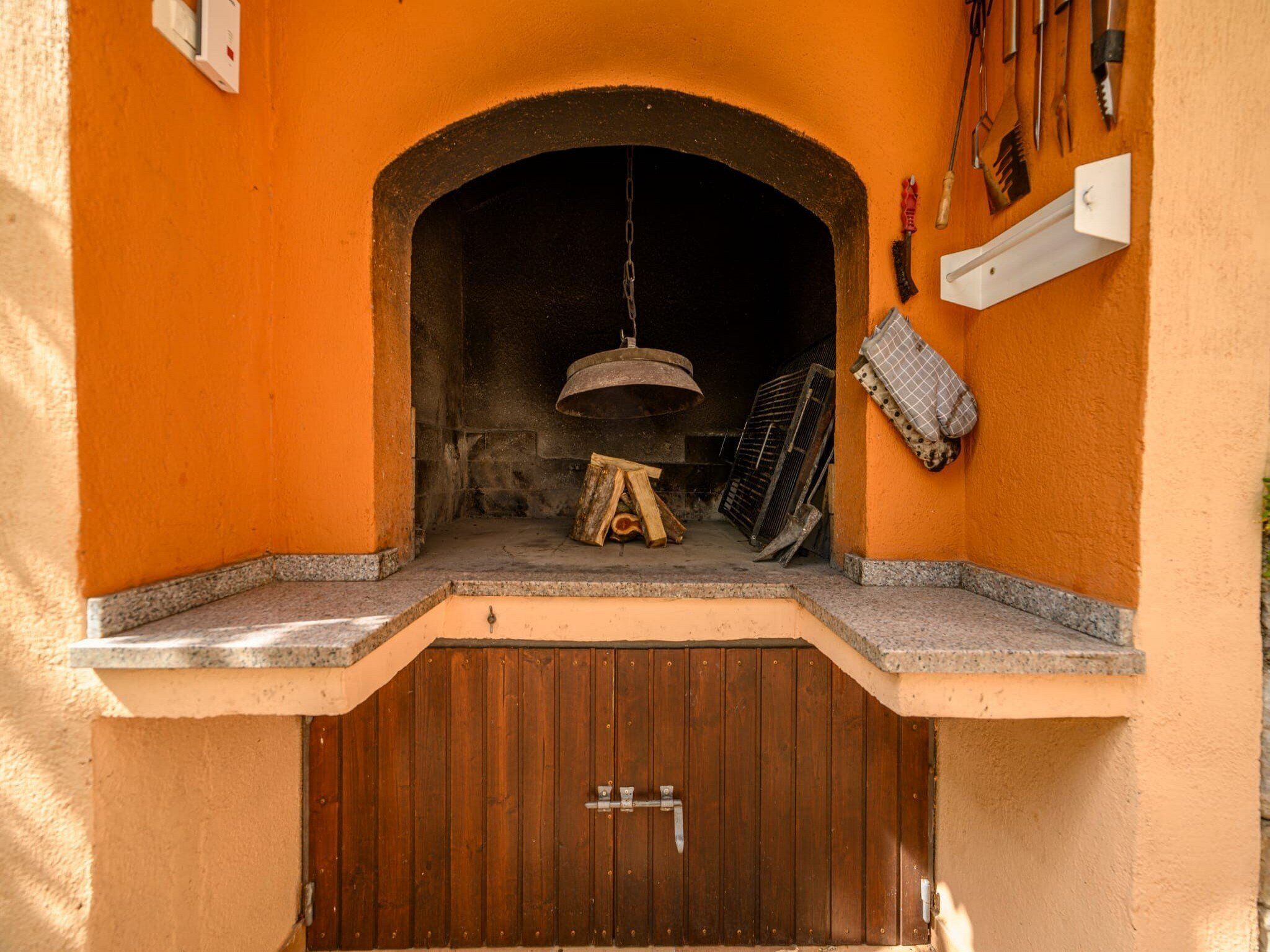 Un horno de ladrillo al aire libre con puerta de madera, un brasero y un estante con herramientas.