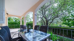 A covered outdoor patio with a glass table and chairs, surrounded by greenery and a large tree. - Holiday Home Rokoko (Sibenik)
