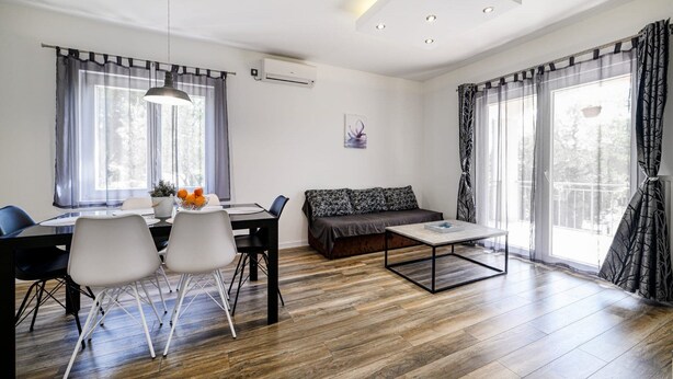 A modern living room with a dining area, wooden flooring, and large windows with curtains. - Holiday Home Rokoko (Sibenik)