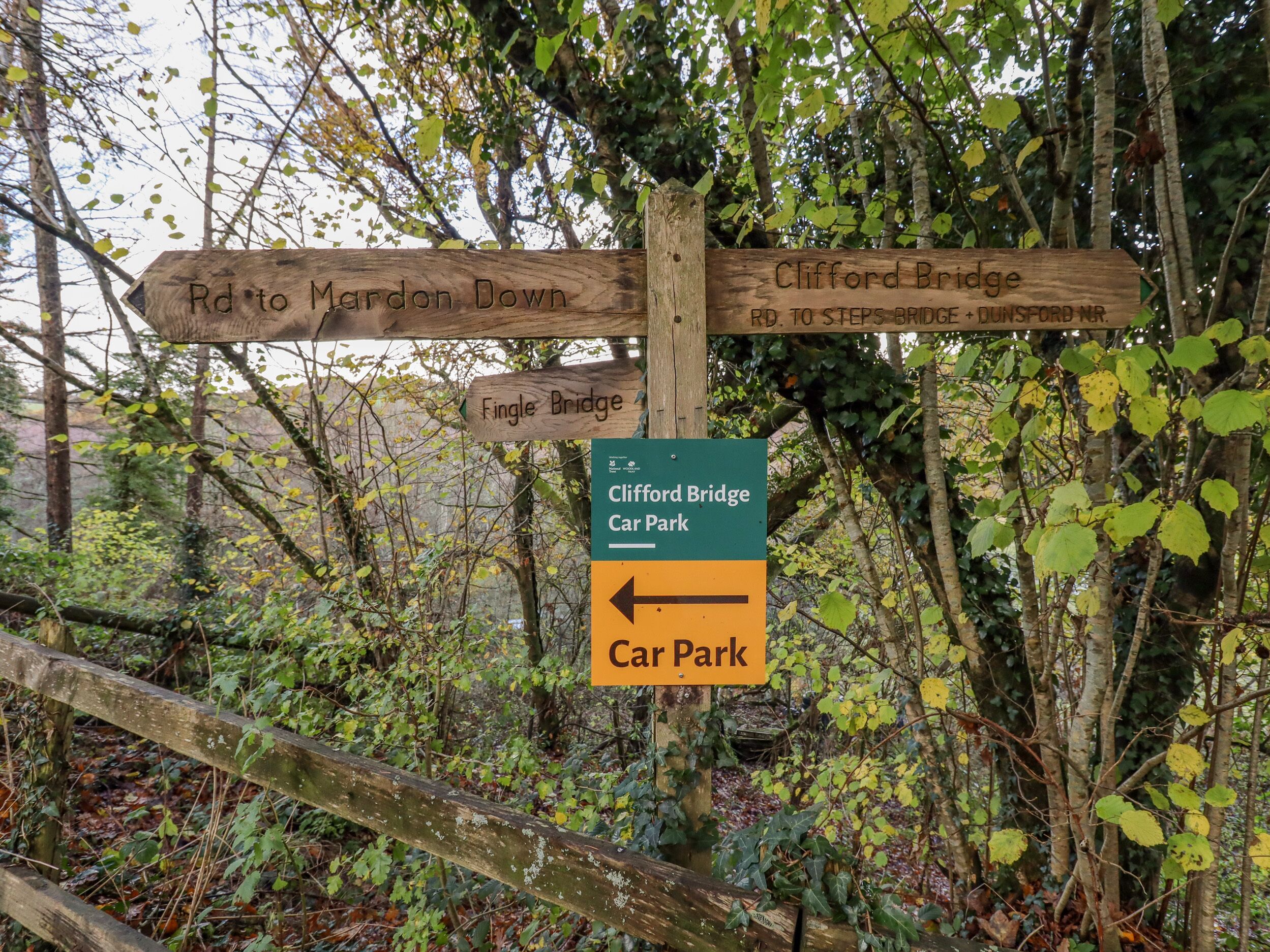 Un cartel de madera con flechas que indican varias direcciones, incluyendo 'Rd to Mardon Down', 'Fingle Bridge' y 'Clifford Bridge'.
