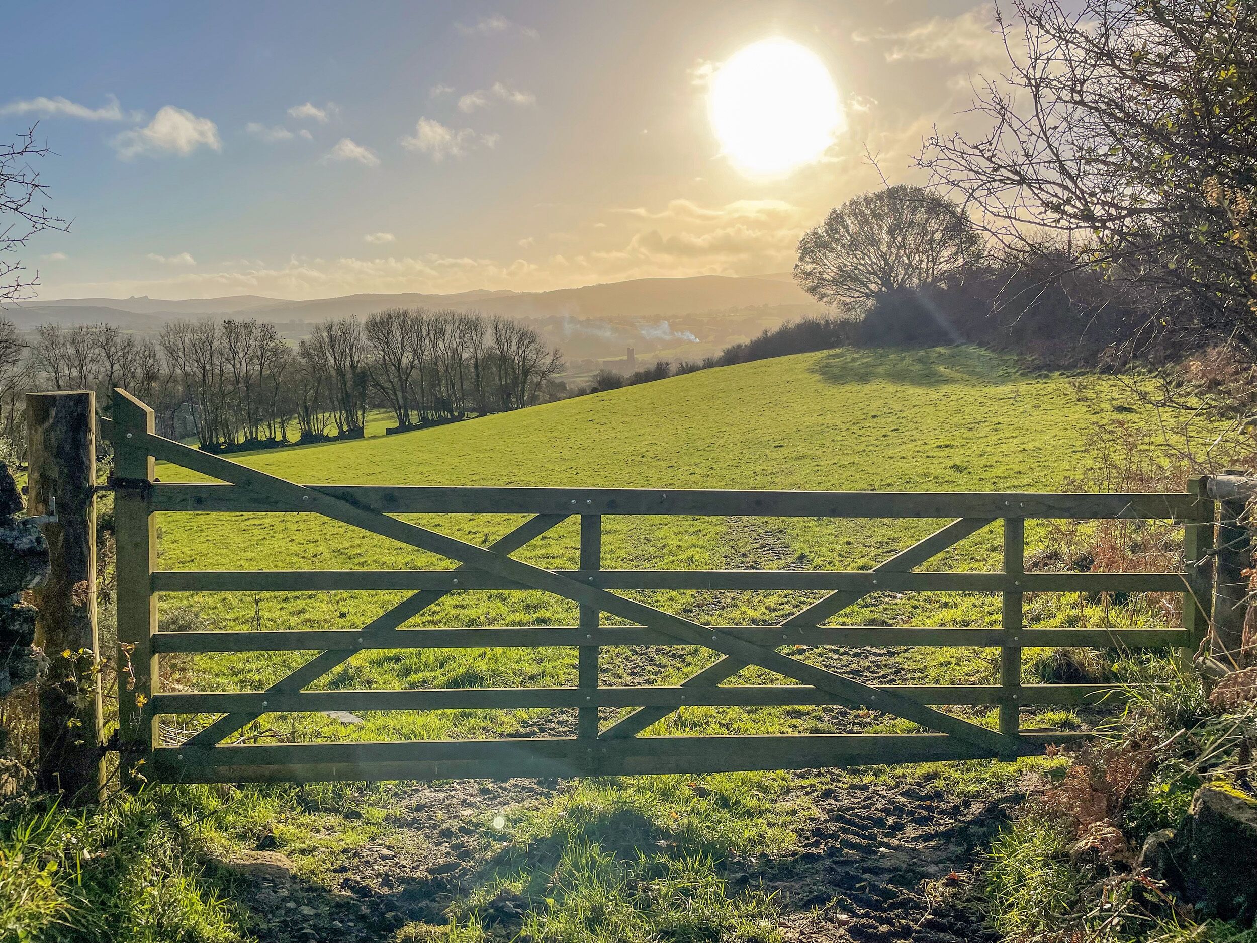 A wooden gate in a rural landscape with a clear sky and distant hills.