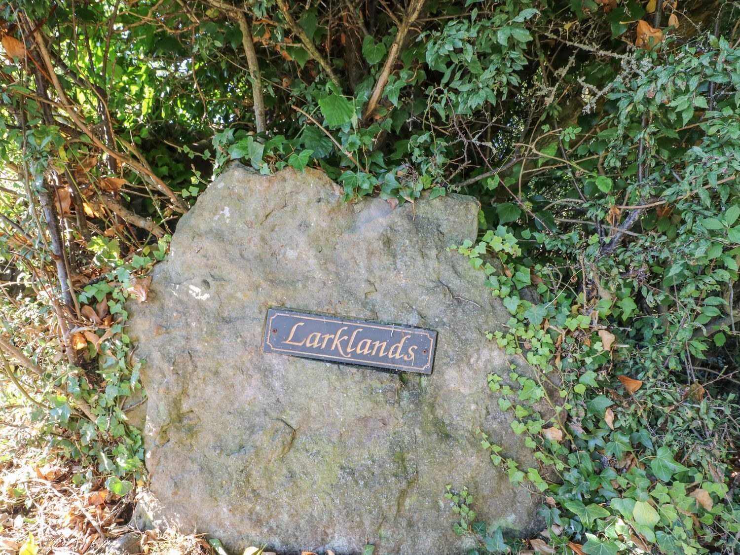 Una grande roccia con un cartello che indica "Larklands", immersa in una vegetazione fitta.