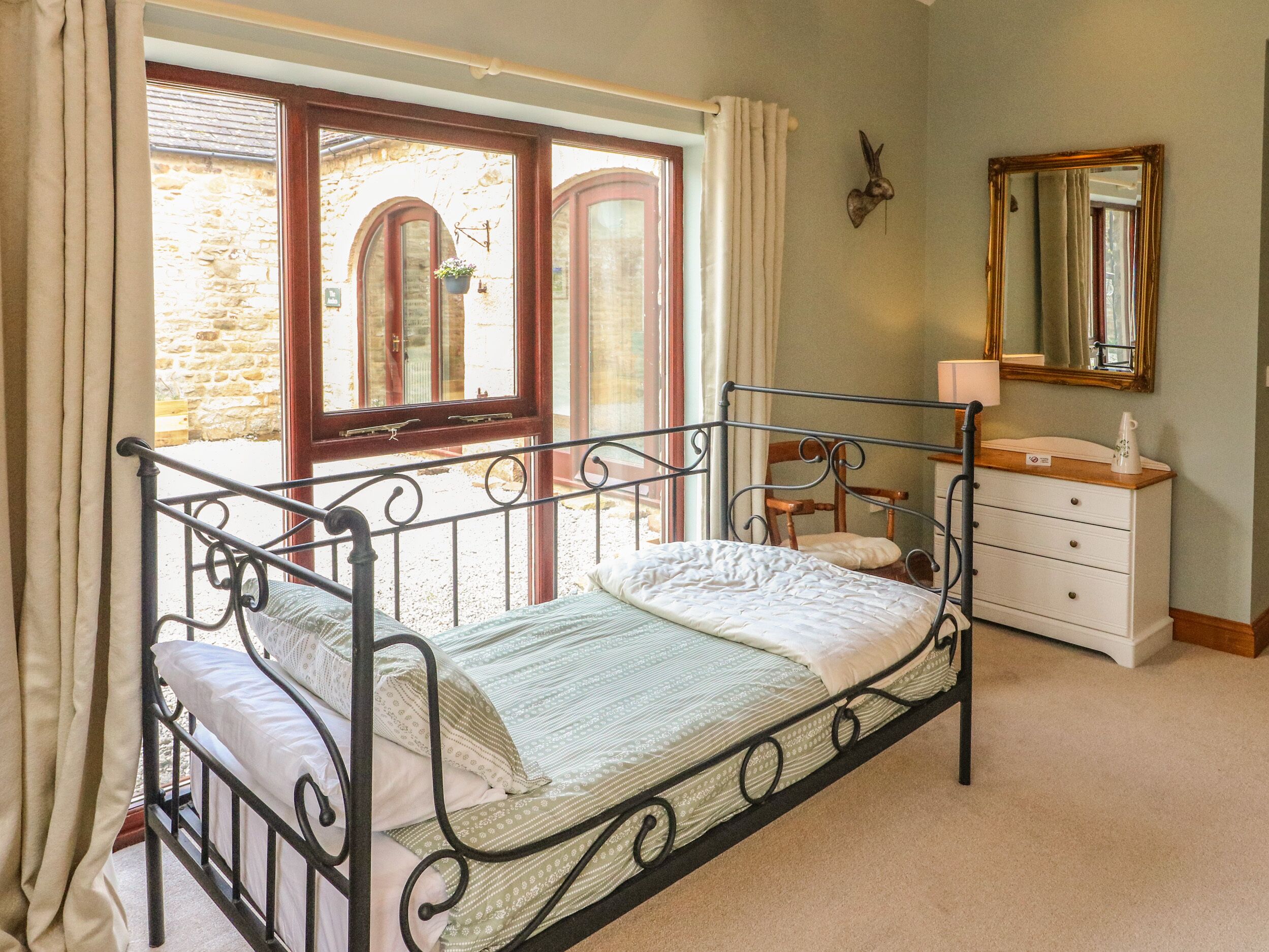 A bedroom with a metal bed frame, a wooden dresser, a mirror, and a window with curtains.