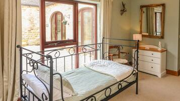 A bedroom with a metal bed frame, a wooden dresser, a mirror, and a window with curtains.