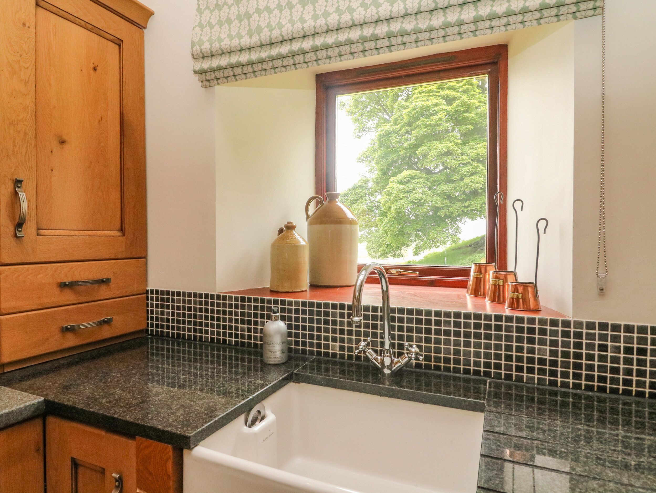 A kitchen with a sink, wooden cabinets, and a window with a view of trees.