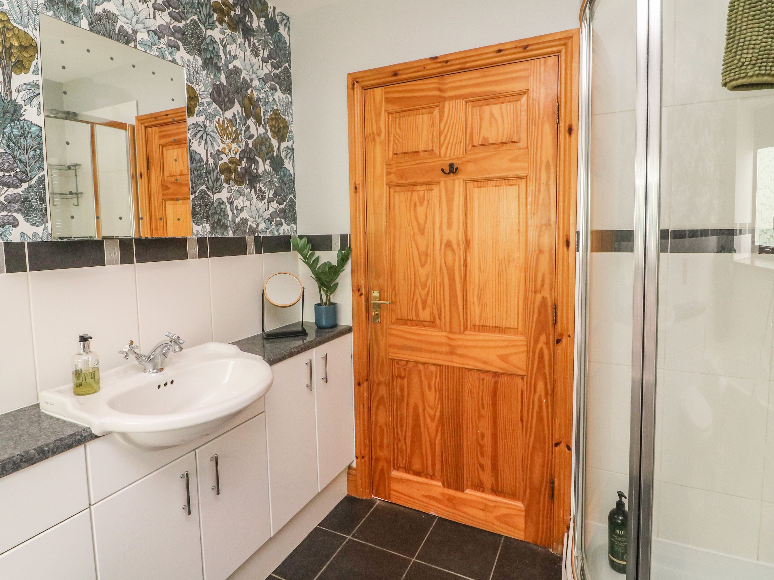 Un baño con puerta de madera, un lavabo con espejo y zona de ducha.