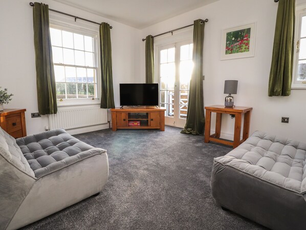 A living room with two grey sofas, a TV on a wooden stand, and a small table with a lamp.