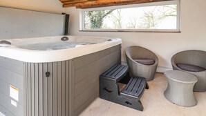 Un área de spa con un jacuzzi, dos sillones de mimbre y una ventana con vista a árboles.
