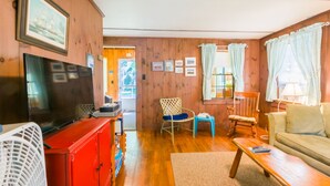 Un salon chaleureux avec des murs en bois, un meuble de rangement rouge, une télévision, un canapé et une fenêtre avec des rideaux.