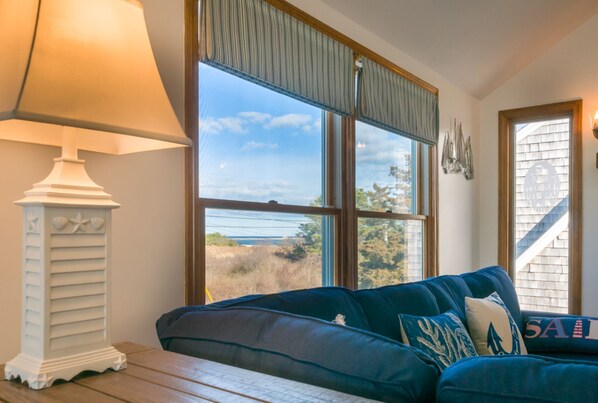 A living room with a large window, a lamp, and a sofa with decorative pillows.