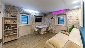 Une pièce chaleureuse avec un mur en pierre, un plancher en bois, un canapé blanc, une petite table avec deux chaises et une bibliothèque remplie de livres.