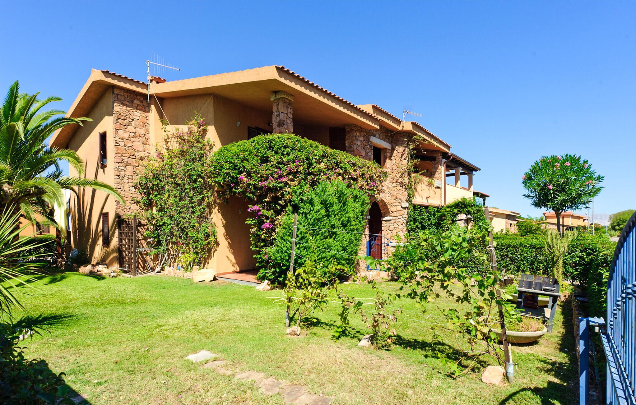 A two-story house with a stone facade, a balcony, and a well-maintained garden with various plants and a lawn.