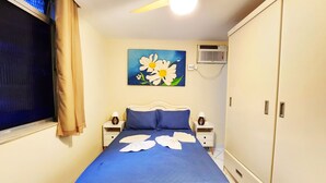 A bedroom with a bed, two bedside tables, a nightstand, a ceiling fan, a painting, an air conditioning unit, and a wardrobe. - Leblon Comfort Suite (Rio de Janeiro)