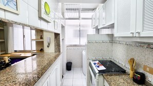 A narrow kitchen with white cabinets, a granite countertop, and a tiled backsplash. - Leblon Comfort Suite (Rio de Janeiro)