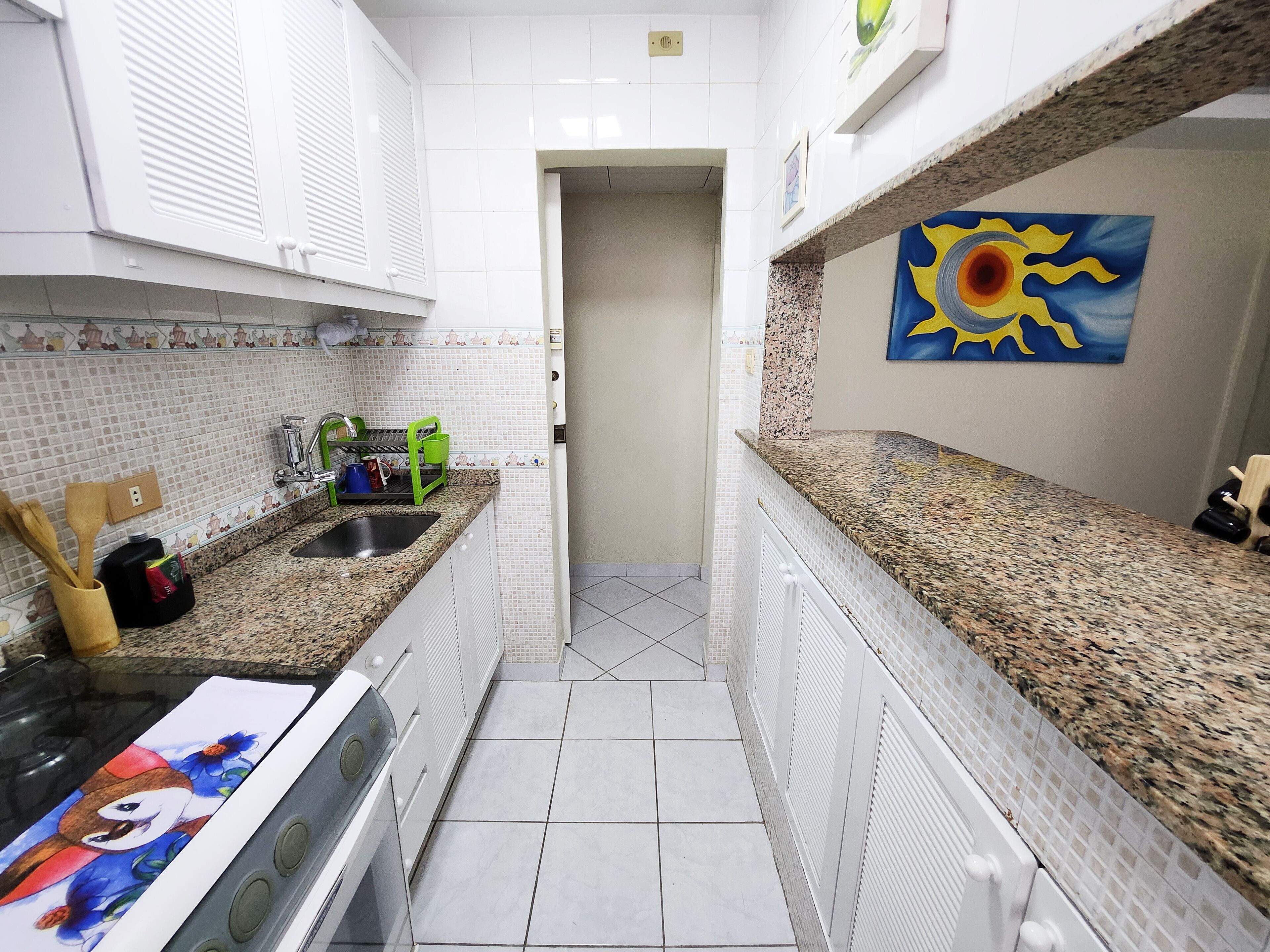 A narrow kitchen with white tiled walls, a granite countertop, and a stainless steel sink.