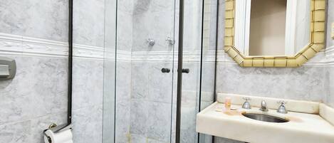 Un baño con ducha de vidrio, un lavabo blanco con espejo y un inodoro.