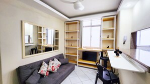 A compact living space with a sofa, a desk, a chair, a mirror, and built-in shelving. - Leblon Comfort Suite (Rio de Janeiro)