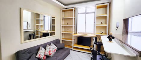 Un espacio habitable compacto con sofá, escritorio, silla, espejo y estanterías empotradas.