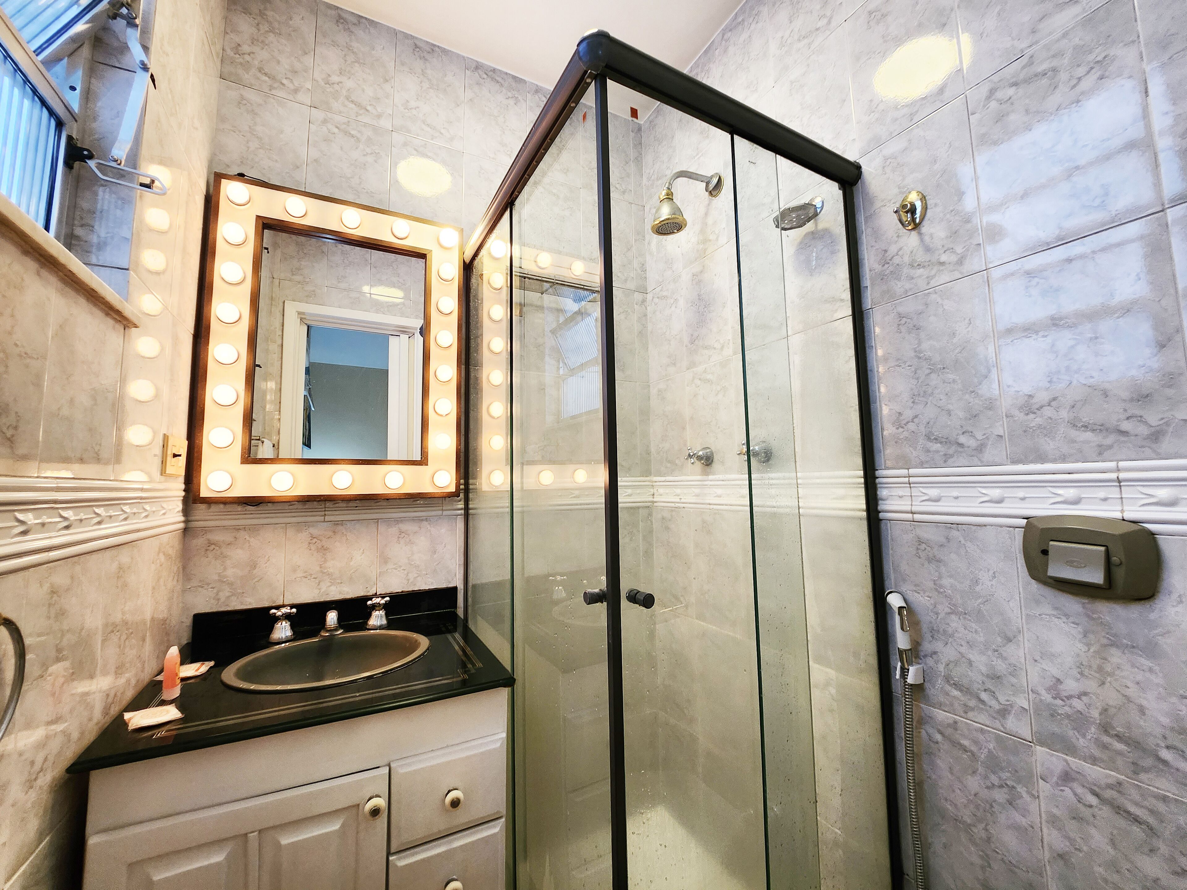A bathroom with a glass-enclosed shower, a vanity with a sink, and a mirror with lights.