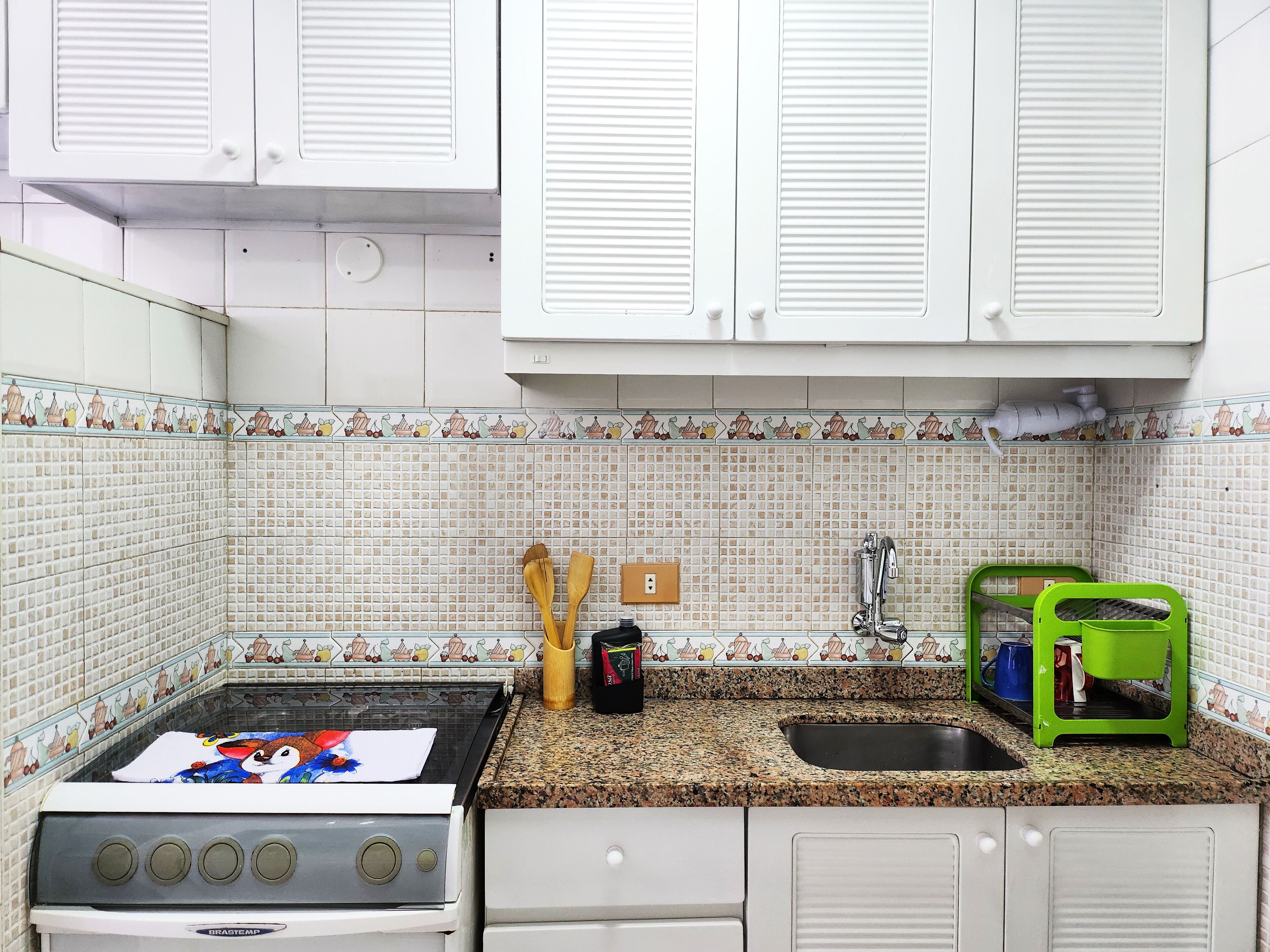 A kitchen with white cabinets, a stove, a sink, and a green dish rack.