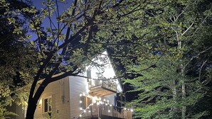 Een huis met balkon, omgeven door groen en een stenen muur.