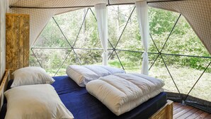 A tented room with a bed, pillows, and a view of greenery.
