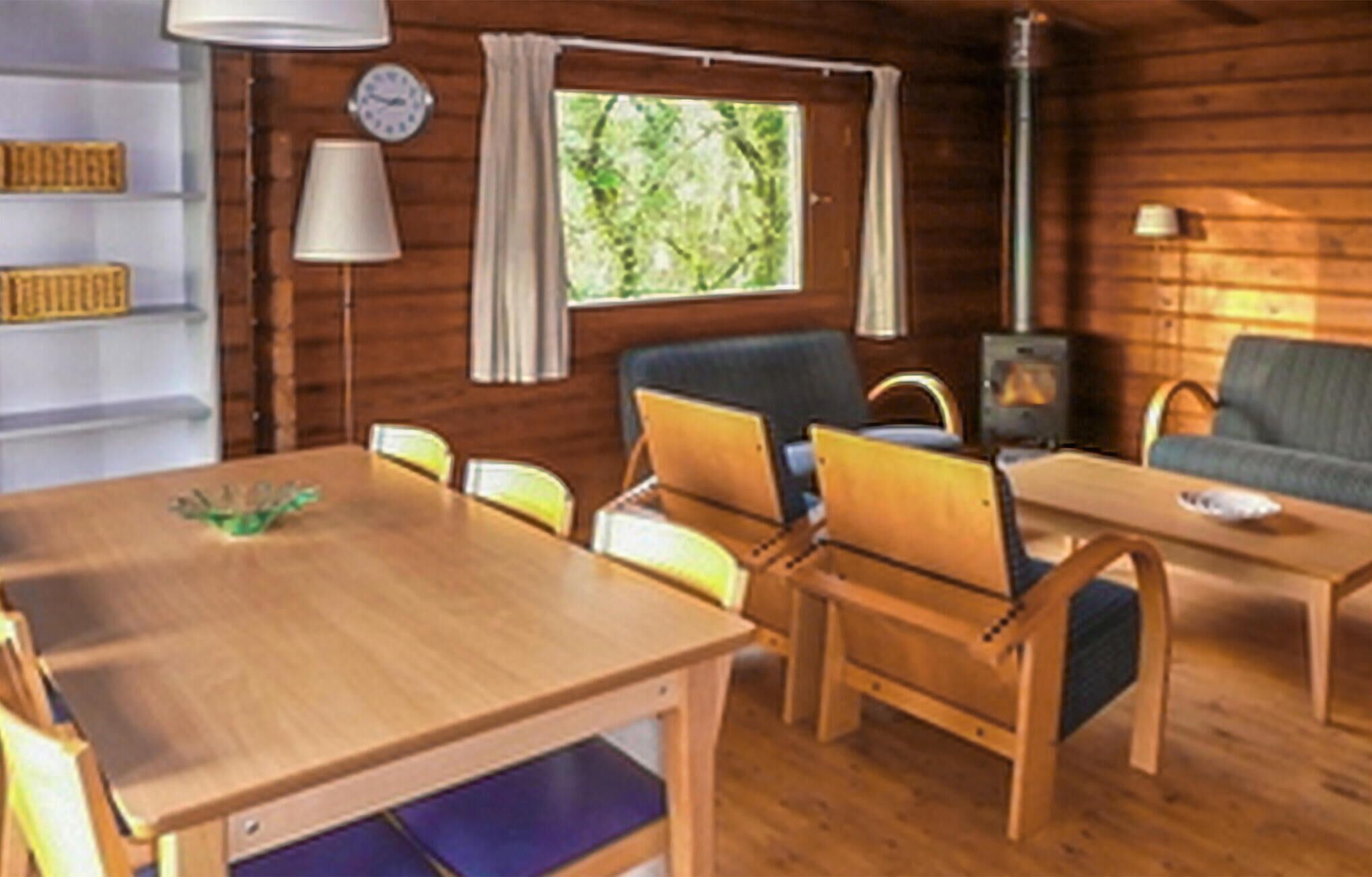 A cozy cabin interior with a wooden dining table, chairs, a sofa, and a fireplace.