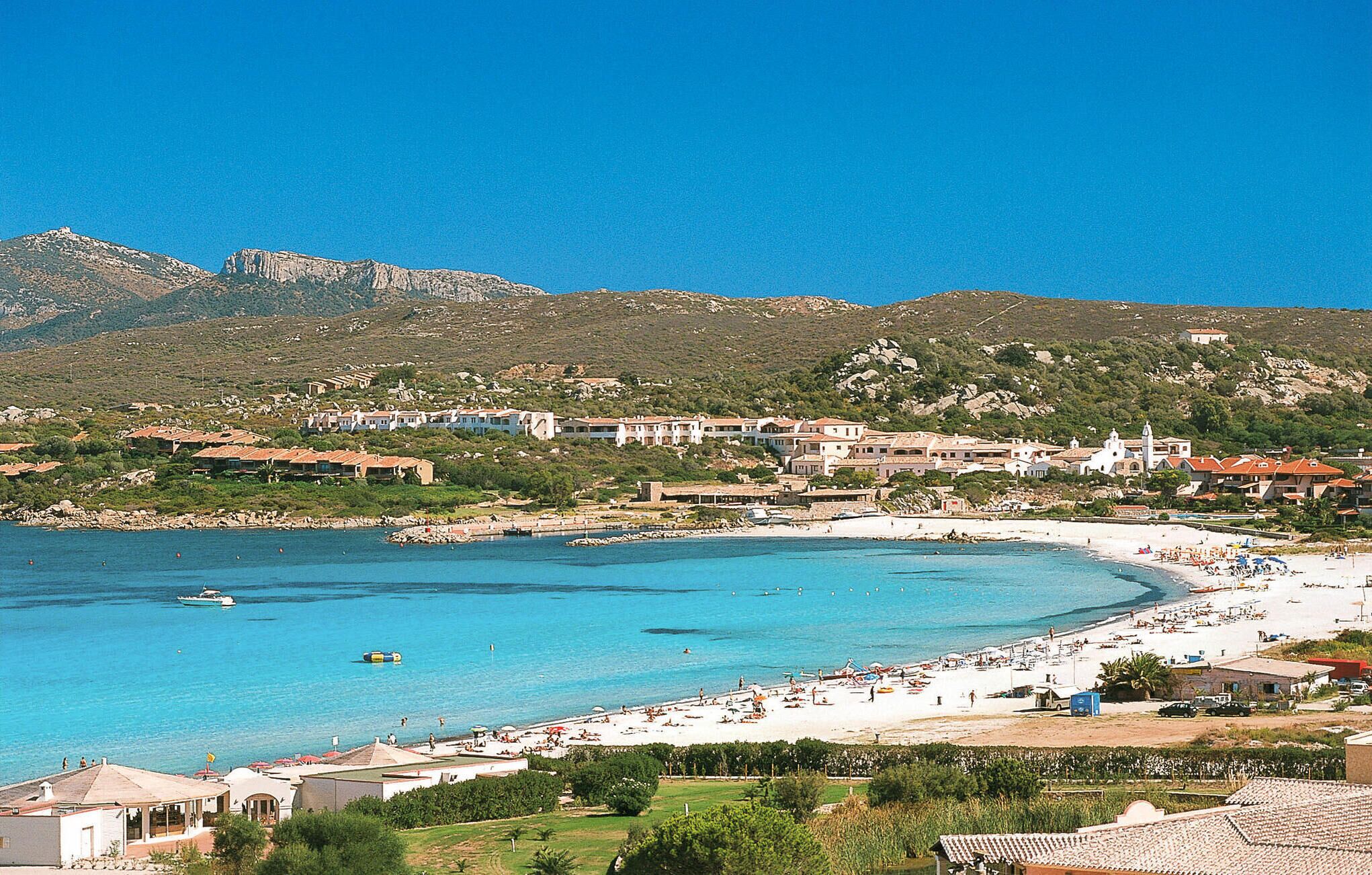 A coastal town with a beach, buildings, and a mountainous backdrop.